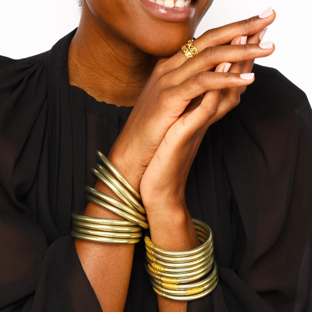 Person wearing gold bracelets and a ring on a plain background